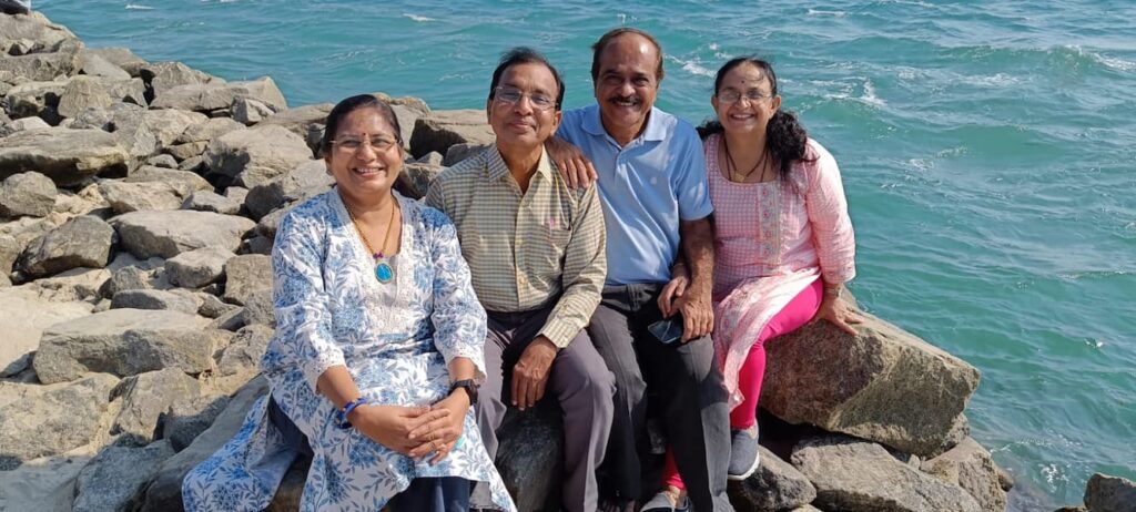 Dr Vijay Karmarkar with his wife Veena and family friends sitting on seaside rocks beside blue sea water